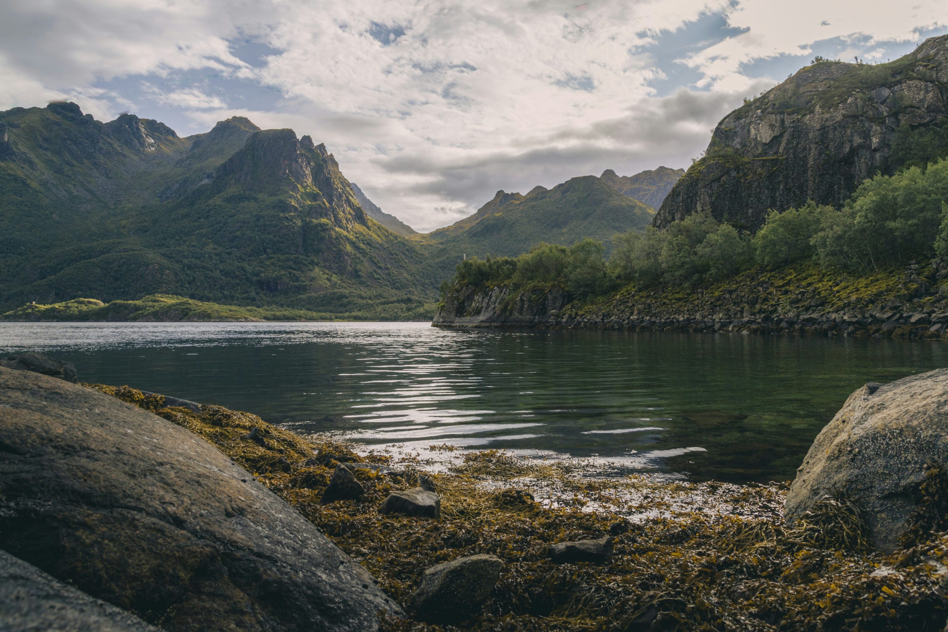 Tranquil lake surrounded by towering mountains under a cloudy sky.