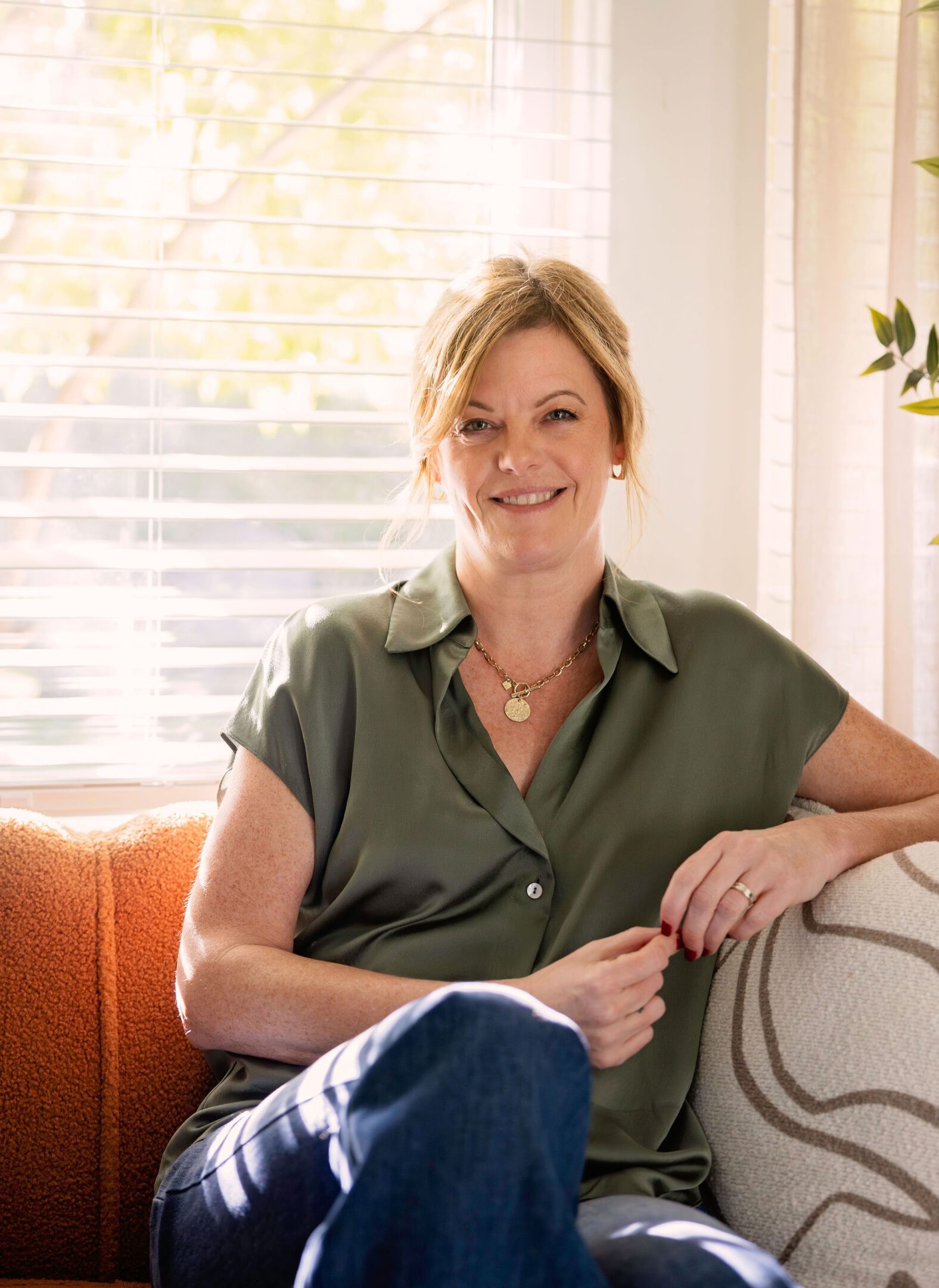 Smiling woman sitting on a couch in a sunlit room.