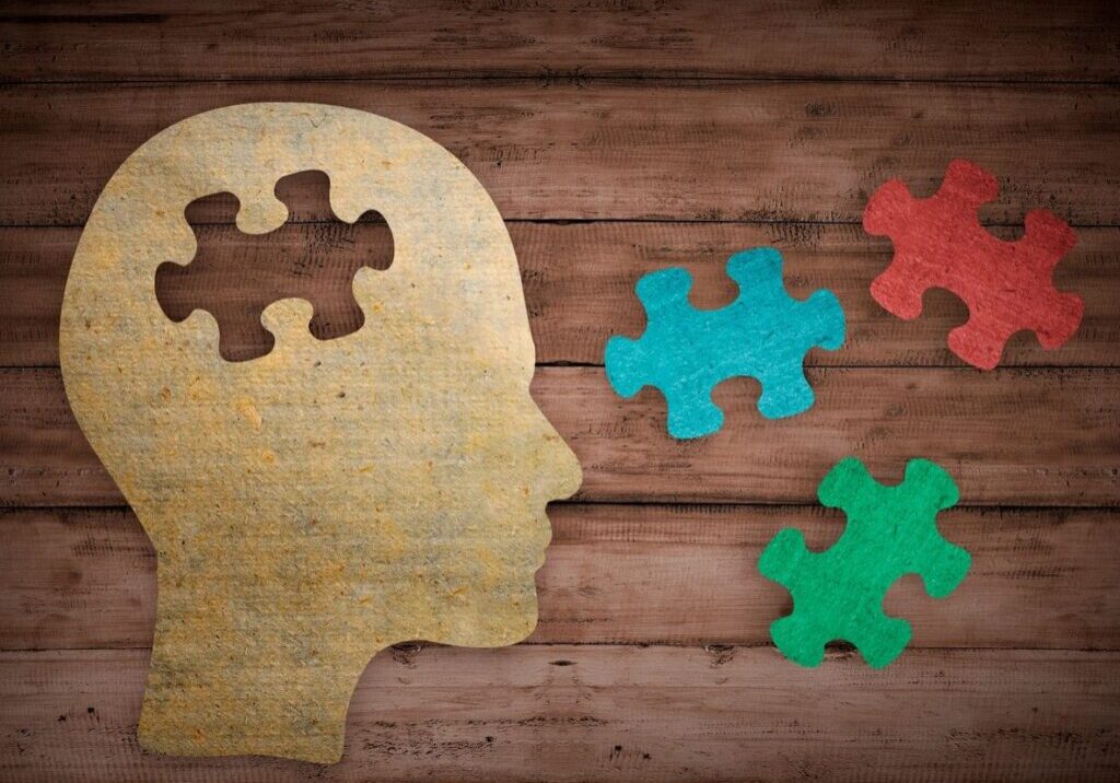 Wooden head silhouette with colorful puzzle pieces symbolizing mental health.